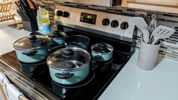 Una cocina con estufa, ollas, una botella de detergente para platos y un recipiente para utensilios.