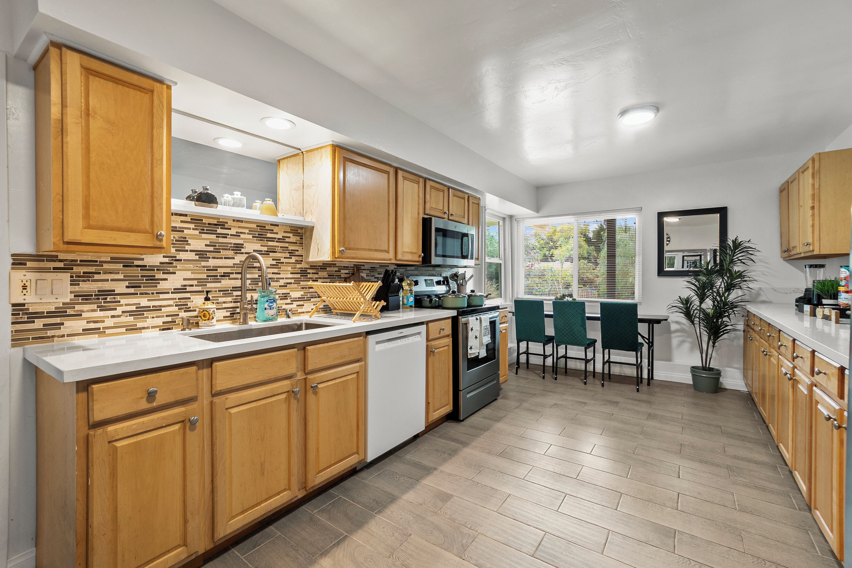 A modern kitchen with wooden cabinets, a tiled backsplash, stainless steel appliances, and a dining area with a view.
