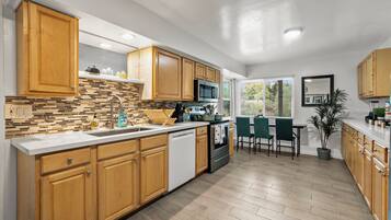 A modern kitchen with wooden cabinets, a tiled backsplash, stainless steel appliances, and a dining area with a view.