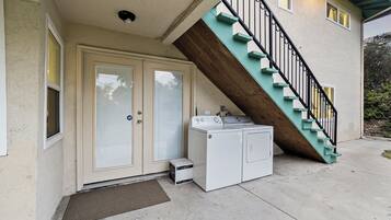 Un edificio residencial con una puerta principal, una escalera con escalones color turquesa y una lavadora afuera.