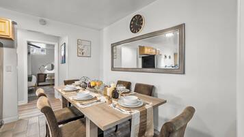 Un comedor con una mesa de madera preparada para cuatro personas, rodeada de sillas. Un espejo grande cuelga en la pared sobre la mesa.