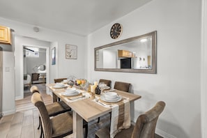 A dining area with a wooden table set for four, surrounded by chairs. A large mirror hangs on the wall above the table. - Entire Private Home w/ 4BR 3Bath, King Bed, Large Yard & Prime Area, Ranch Style (La Mesa)