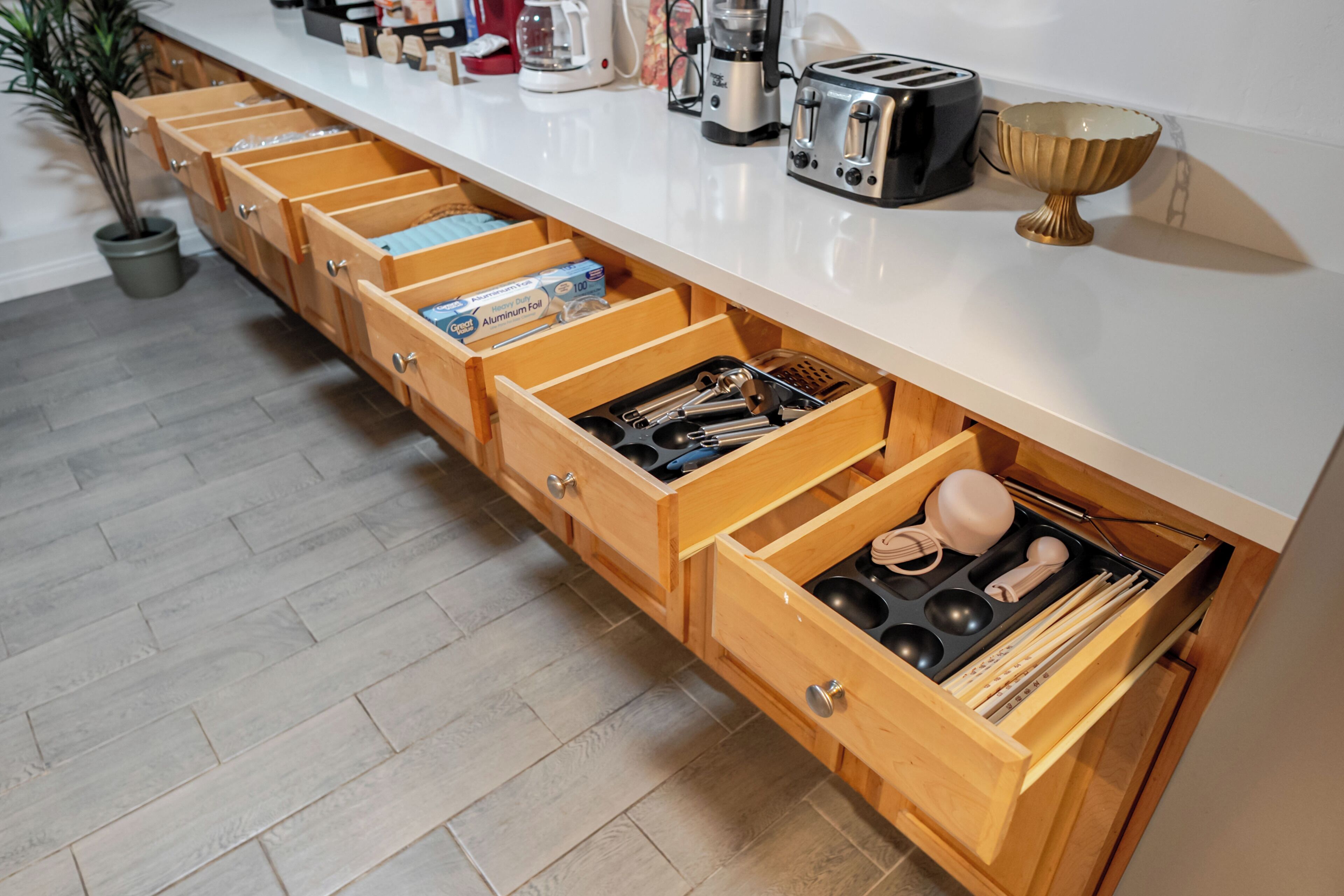 A kitchen with multiple wooden drawers, a white countertop, and various kitchen appliances.