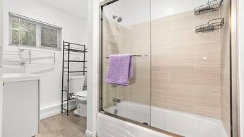 Un baño moderno con ducha de vidrio, lavamanos blanco y retrete.