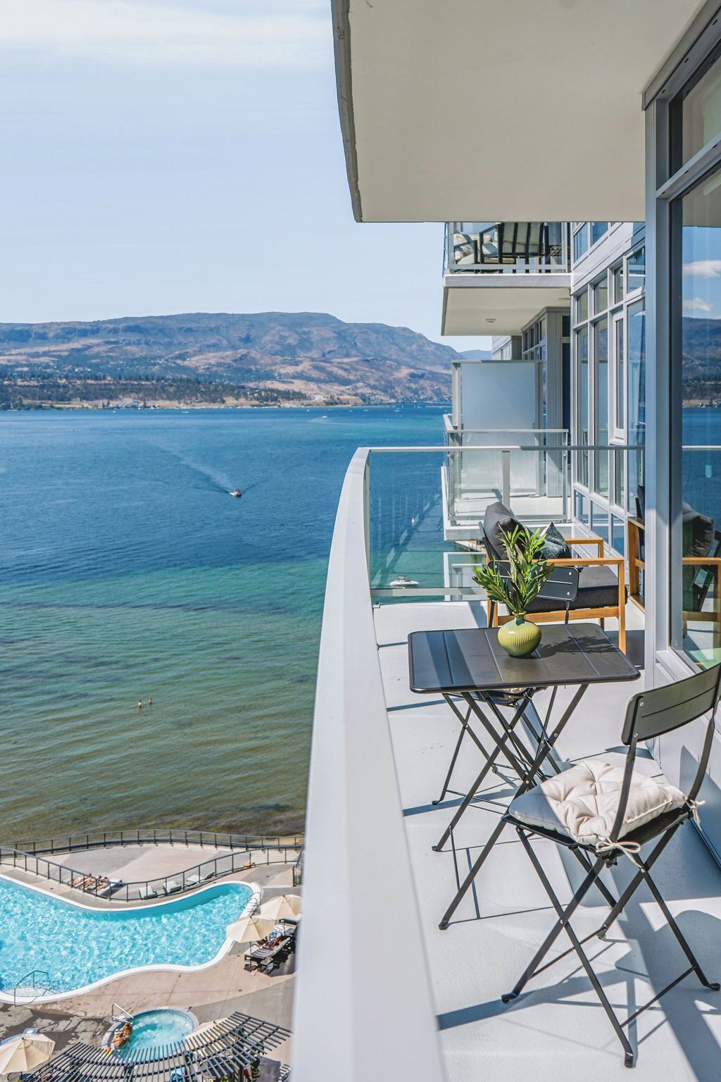 Ein Balkon mit Blick auf einen See und Berge, einen Pool sowie Gartenmöbel.