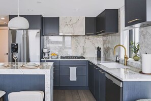 Een moderne keuken met donkere kastjes, een marmeren spatwand en roestvrijstalen apparatuur.