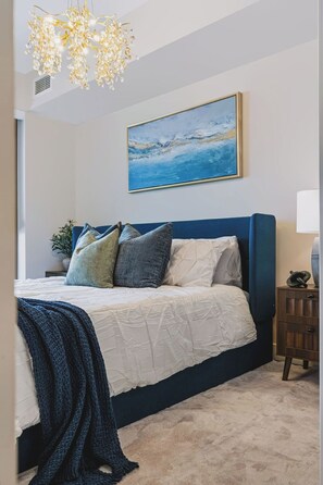 A bedroom with a bed, a painting, a nightstand, and a chandelier. - Raindance 2BR+2BA | Central DT | Pet-friendly (Kelowna)