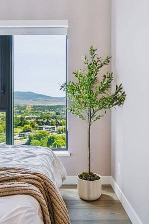 Un dormitori amb una finestra gran, un llit amb un mantell blanc i un arbre en test.