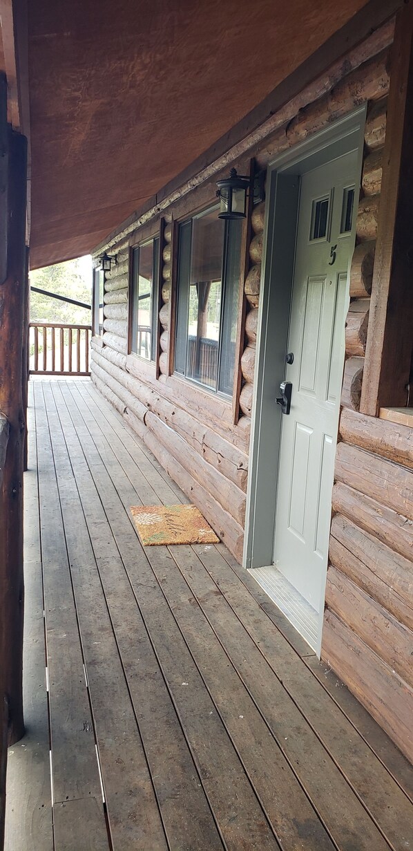 A log cabin with a wooden deck, a white door with the number 5, and a lantern on the wall.