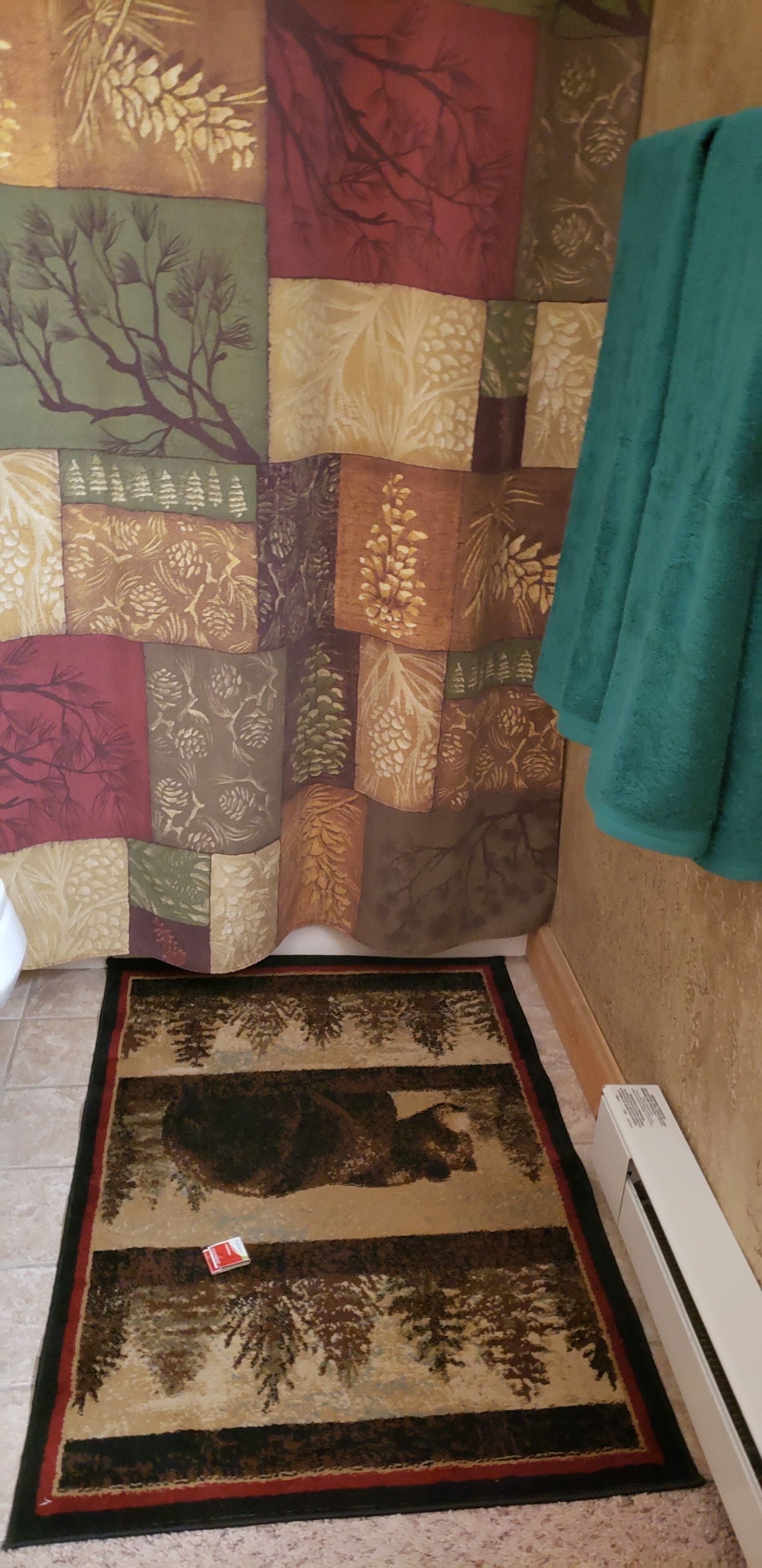 A bathroom with a patterned shower curtain, a rug with a forest design, and a towel hanging on the wall.