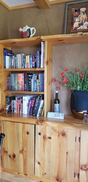 A wooden bookshelf with books, a bottle, and a vase with red flowers. - Charming 1-bedroom condo in peaceful Condon perfect for relaxing getaway (Condon)
