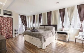 Une chambre à coucher avec un grand lit, une table de chevet, une commode et une fenêtre avec des rideaux.