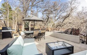 Une terrasse extérieure équipée d’un barbecue, d’une table à manger, de chaises et d’une table avec un plateau en verre.