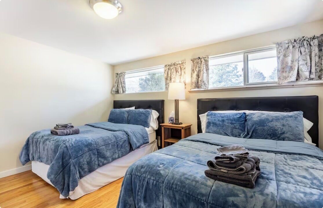 A bedroom with two beds, a nightstand, and a window with curtains.