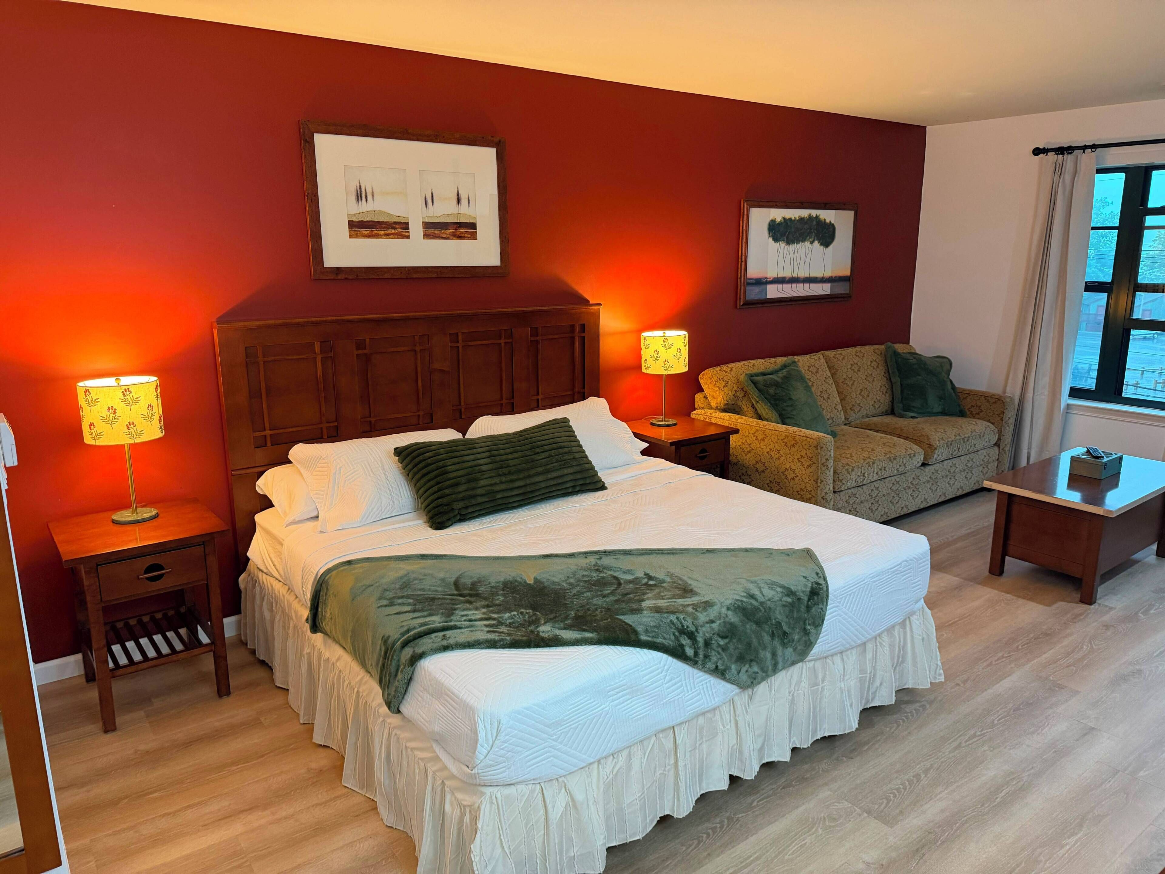 Habitación de hotel con una cama grande, un sofá, dos mesitas de noche con lámparas y obras de arte en las paredes.