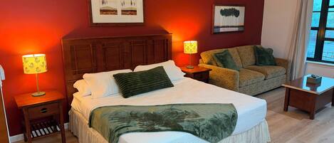 Une chambre d’hôtel avec un grand lit, un canapé, deux tables de chevet avec des lampes et des œuvres d’art accrochées aux murs.
