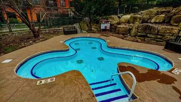 Une piscine à la forme originale, entourée d’un mur de pierre et d’une clôture en métal.