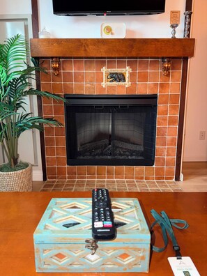 A fireplace with a bear decoration, a television mounted above it, and a remote control on a patterned box.