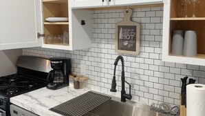 Une cuisine avec des meubles blancs, un évier en acier inoxydable, un plan de travail en marbre et un pare-feu en carrelage blanc.