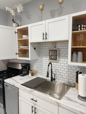 A kitchen with white cabinets, a stainless steel sink, a marble countertop, and a backsplash with white tiles. - Charming 1bedroom Suite 7minutes from Downtown Cleveland (Cleveland)