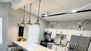 Une cuisine moderne dotée d’un plan de travail en marbre, d’appareils électroménagers en acier inoxydable et de luminaires suspendus.