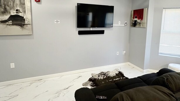 Un salon moderne avec un téléviseur à écran plat fixé au mur, un canapé et un sol à motifs de marbre.