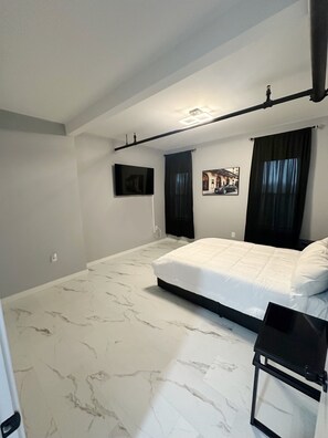 A bedroom with a large bed, a flat-screen TV mounted on the wall, and a ceiling light fixture. - Charming 1bedroom Suite 7minutes from Downtown Cleveland (Cleveland)