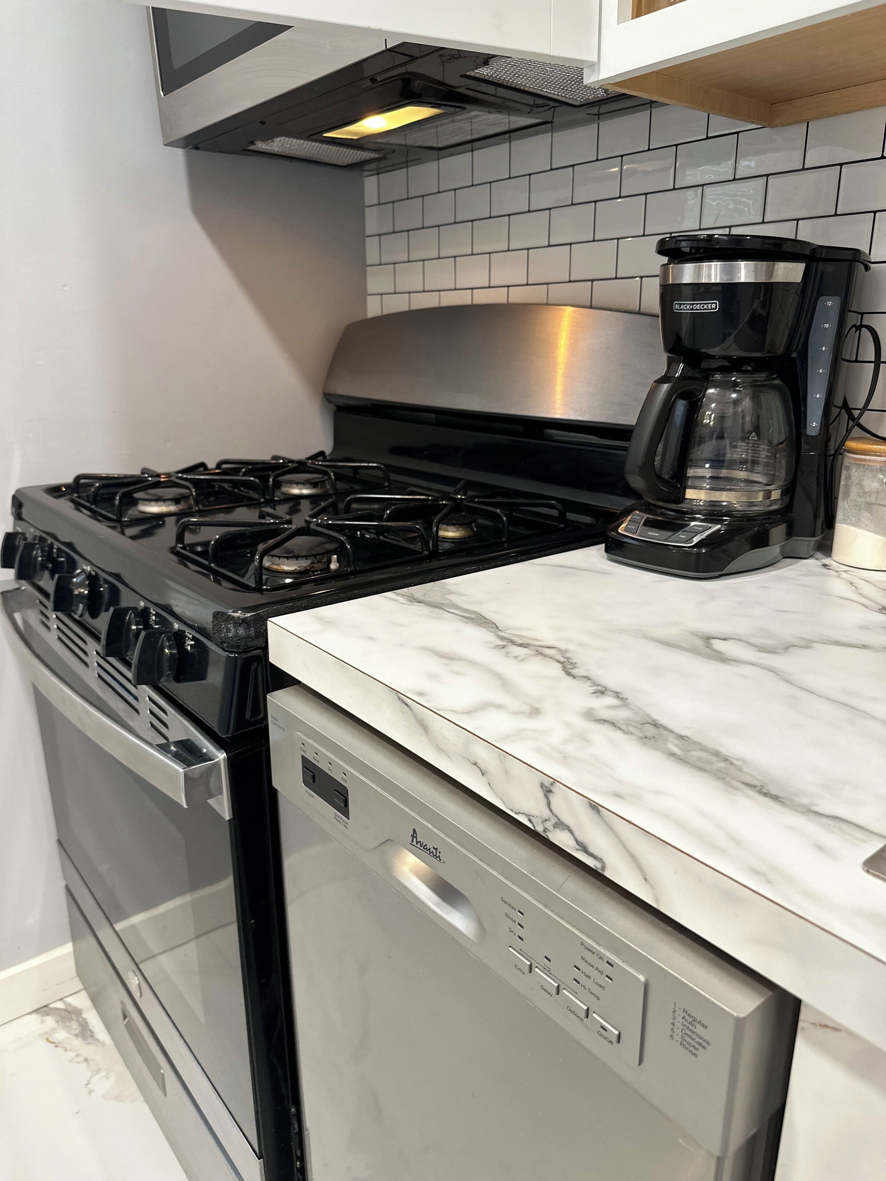 Una cocina con estufa de acero inoxidable, lavavajillas y cafetera sobre la encimera.