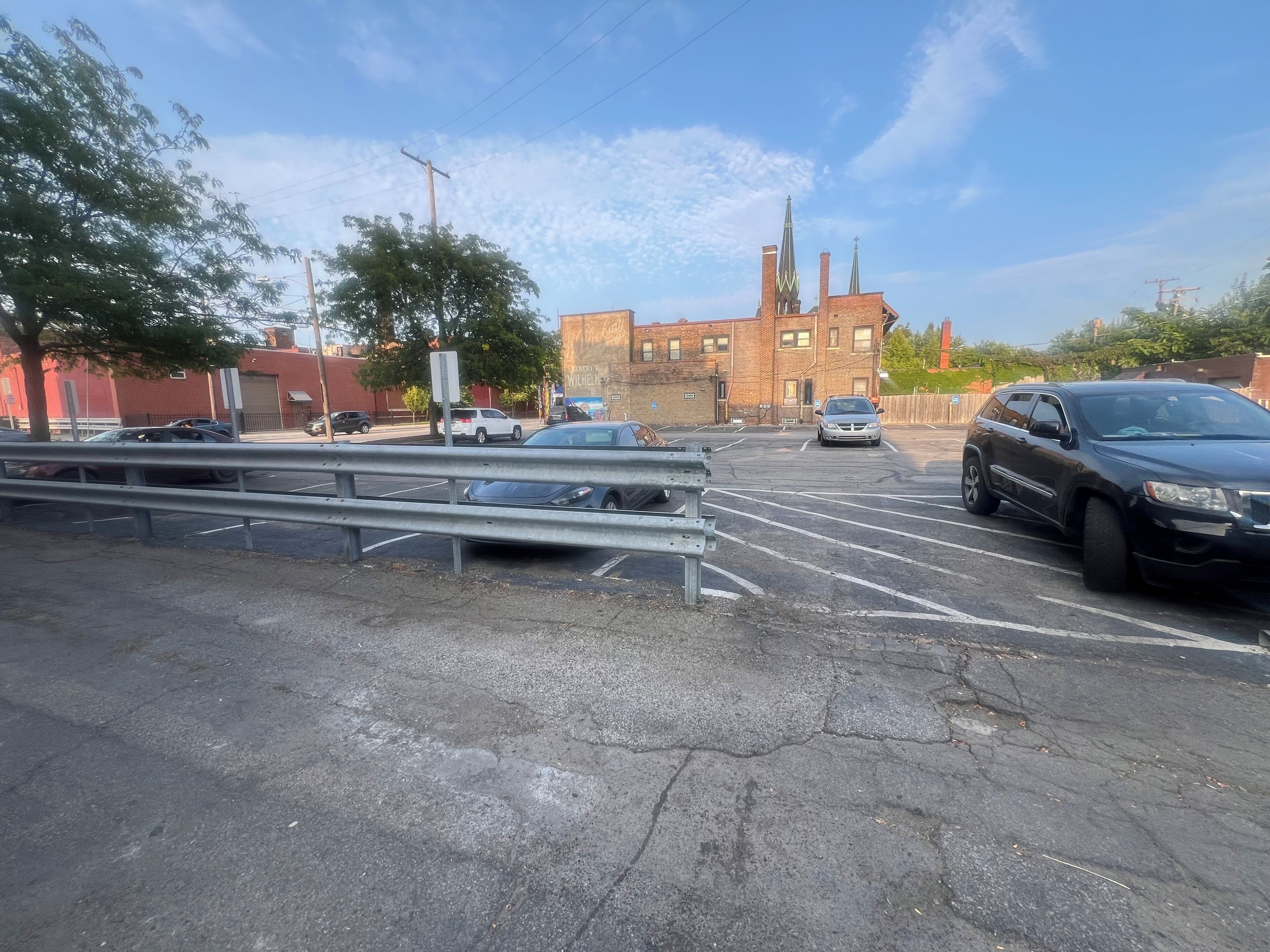 A parking lot with multiple cars, a metal guardrail, and a building with a brick facade in the background.