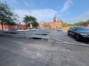 A parking lot with multiple cars, a metal guardrail, and a building with a brick facade in the background.