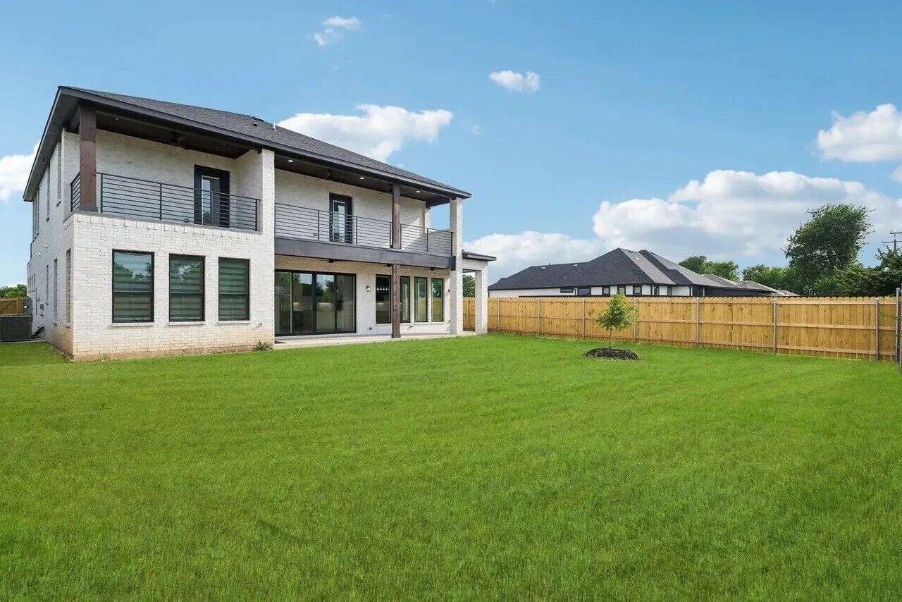 A two-story house with a large backyard, a wooden fence, and a small tree.