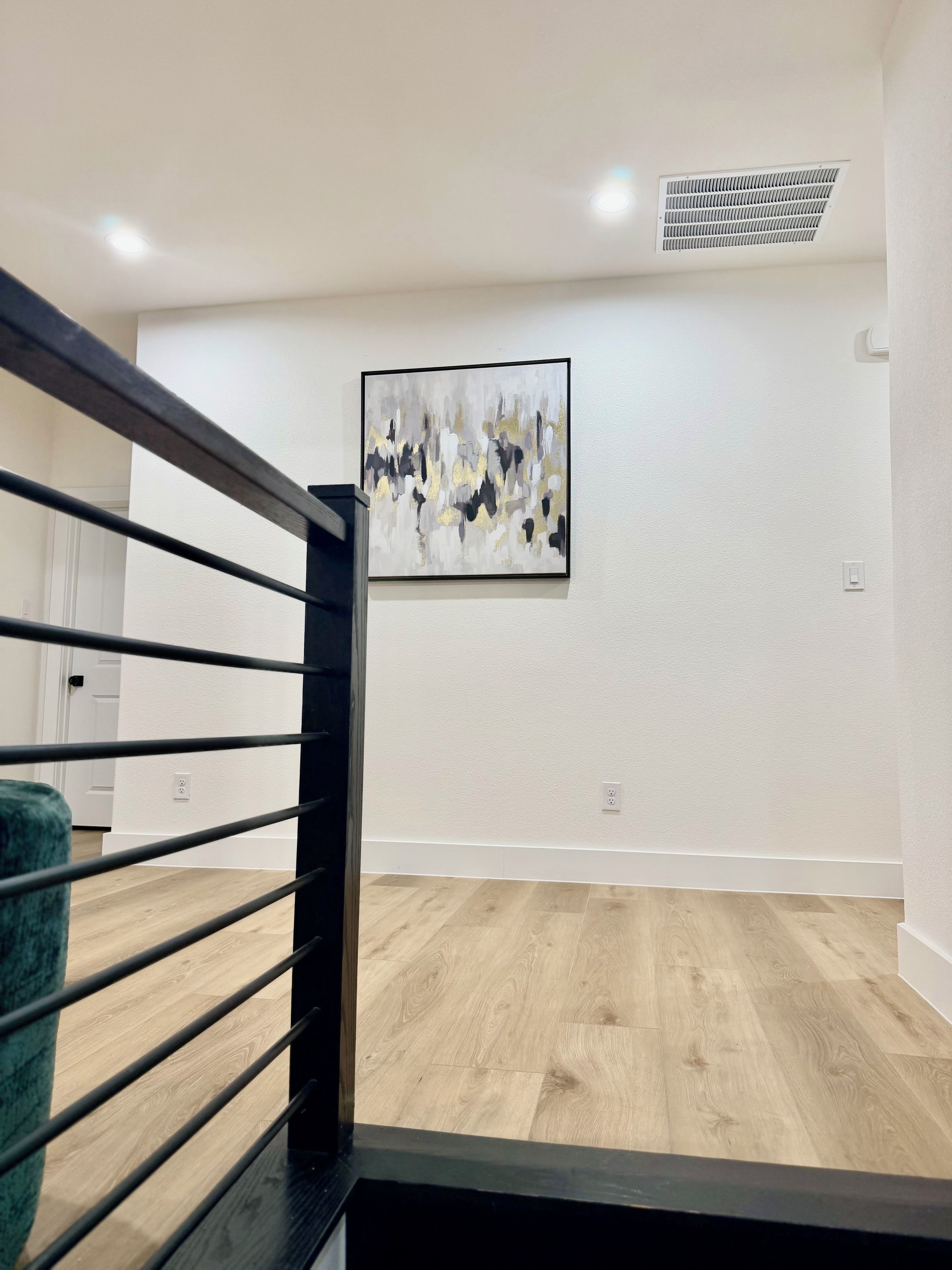 Escada com corrimão preto que leva a um quarto com piso de madeira e parede branca.