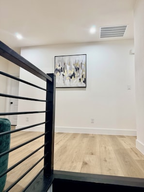 A staircase with a black railing leading to a room with a wooden floor and a white wall.