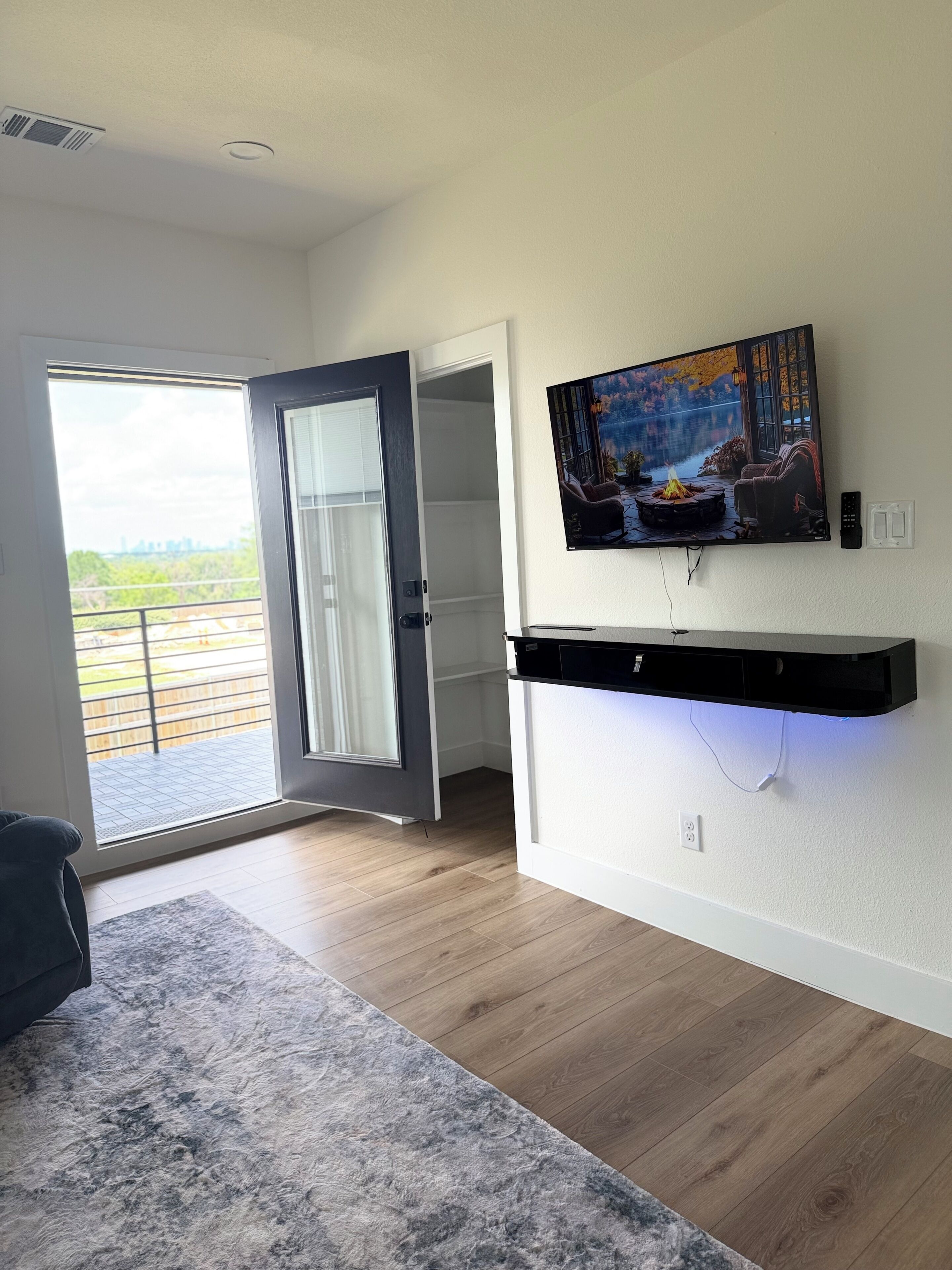 Ein Zimmer mit großem Fenster, einem an der Wand befestigten Flachbildfernseher und Holzboden.