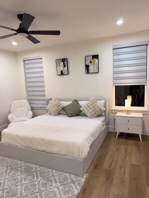 Ein Schlafzimmer mit einem Bett, einem weißen Nachttisch, einem Deckenventilator und zwei an der Wand befestigten Kunstwerken.