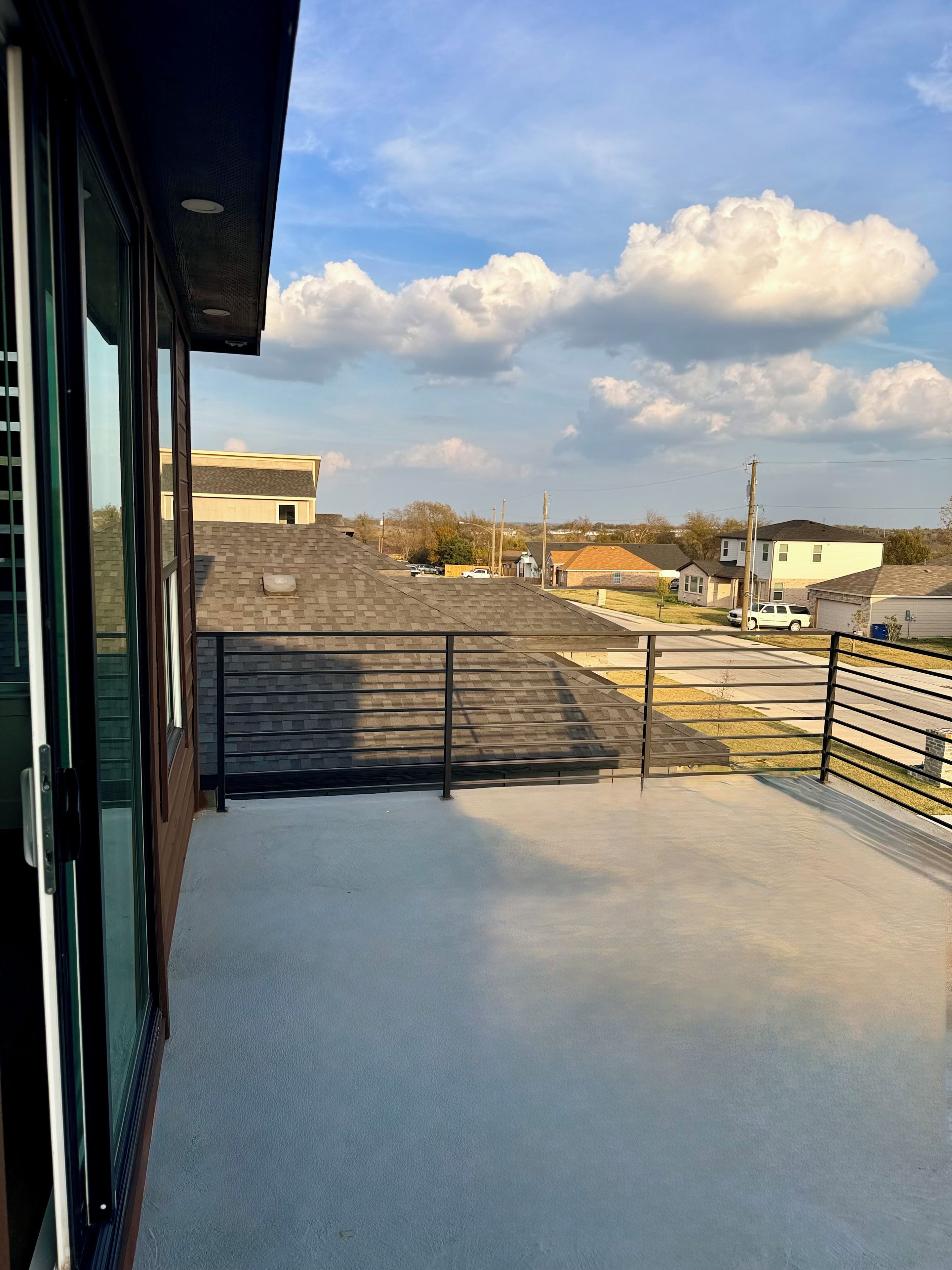 A balcony with a view of a residential neighborhood, including houses and a parking area.