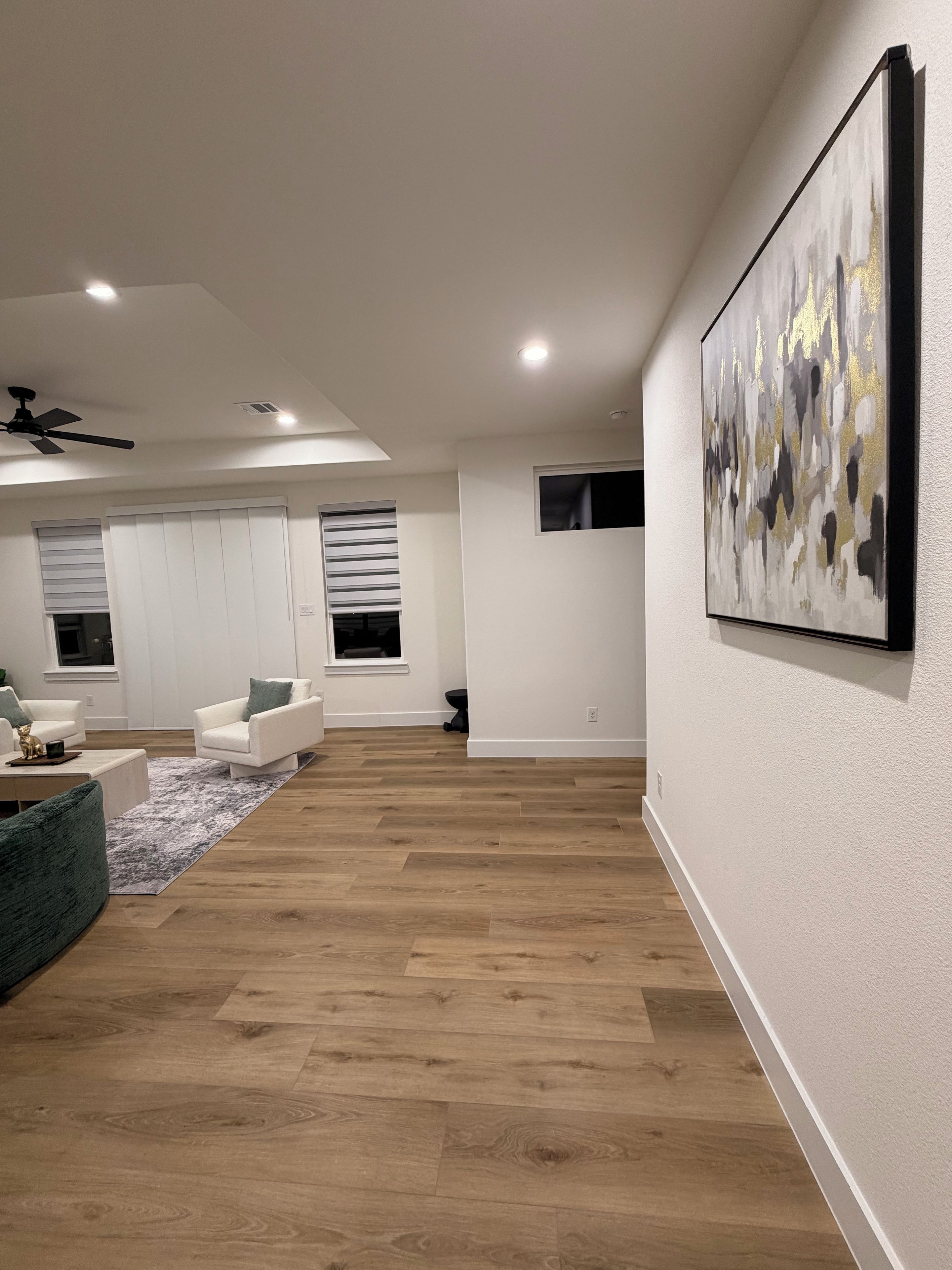 Uma sala de estar moderna com piso de madeira, sofás brancos, um tapete cinza e um ventilador de teto.