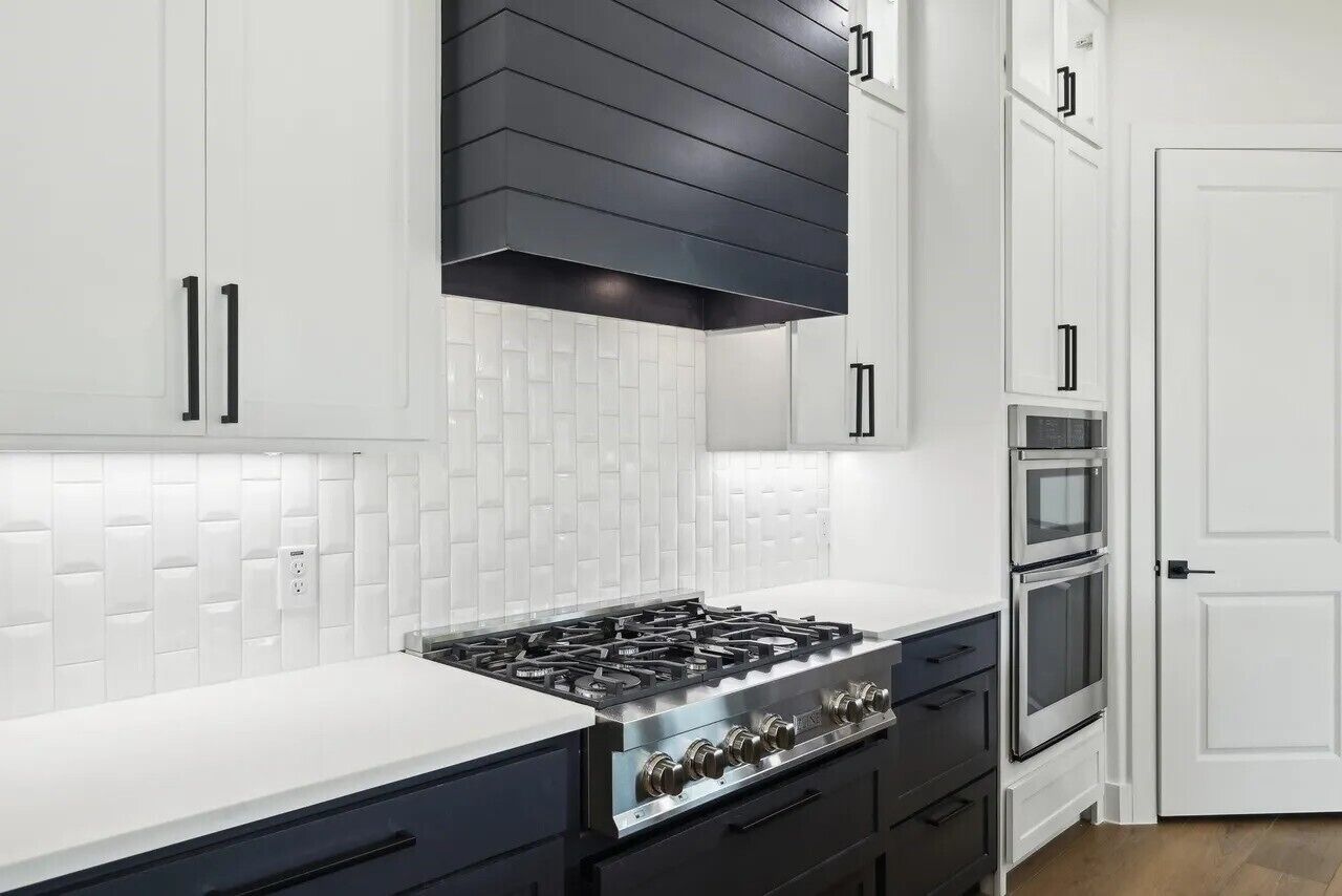Une cuisine moderne avec des armoires blanches, une hotte noire et des appareils électroménagers en acier inoxydable.