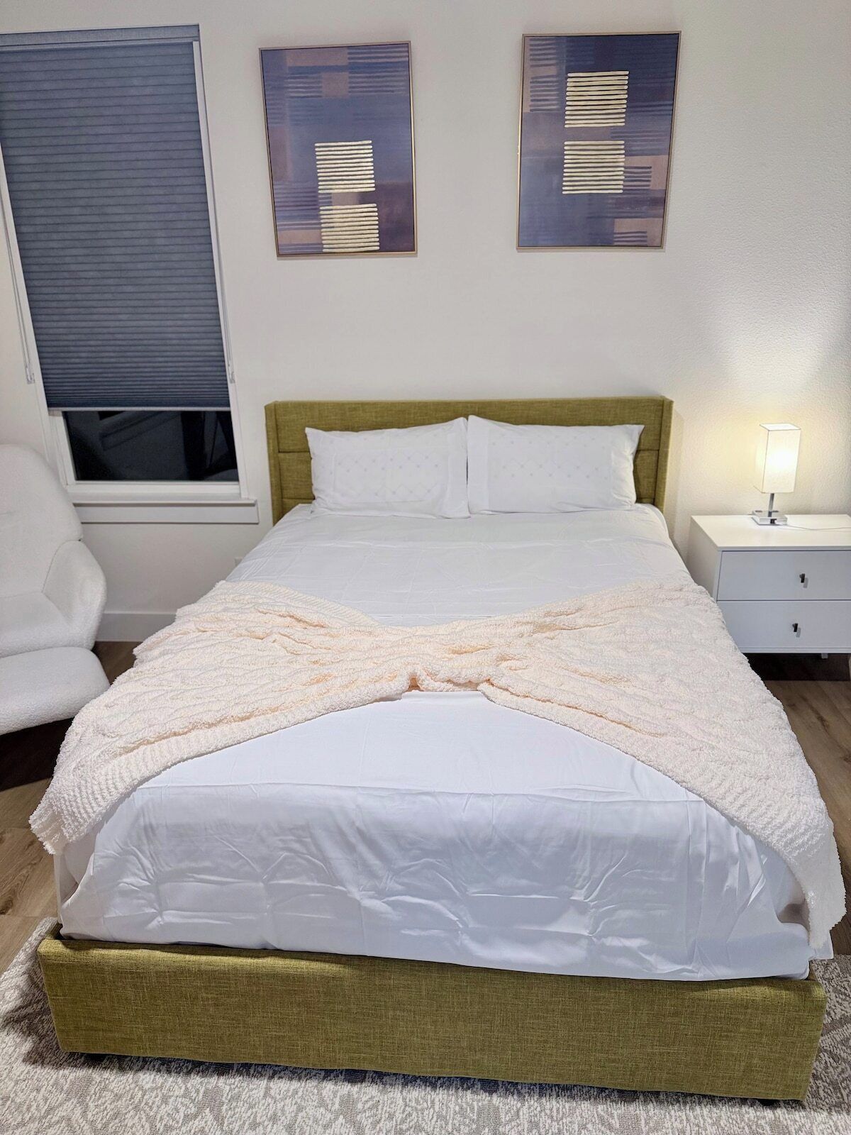 Un lit bien fait, avec une couette blanche, une tête de lit verte et une table de chevet surmontée d’une lampe.