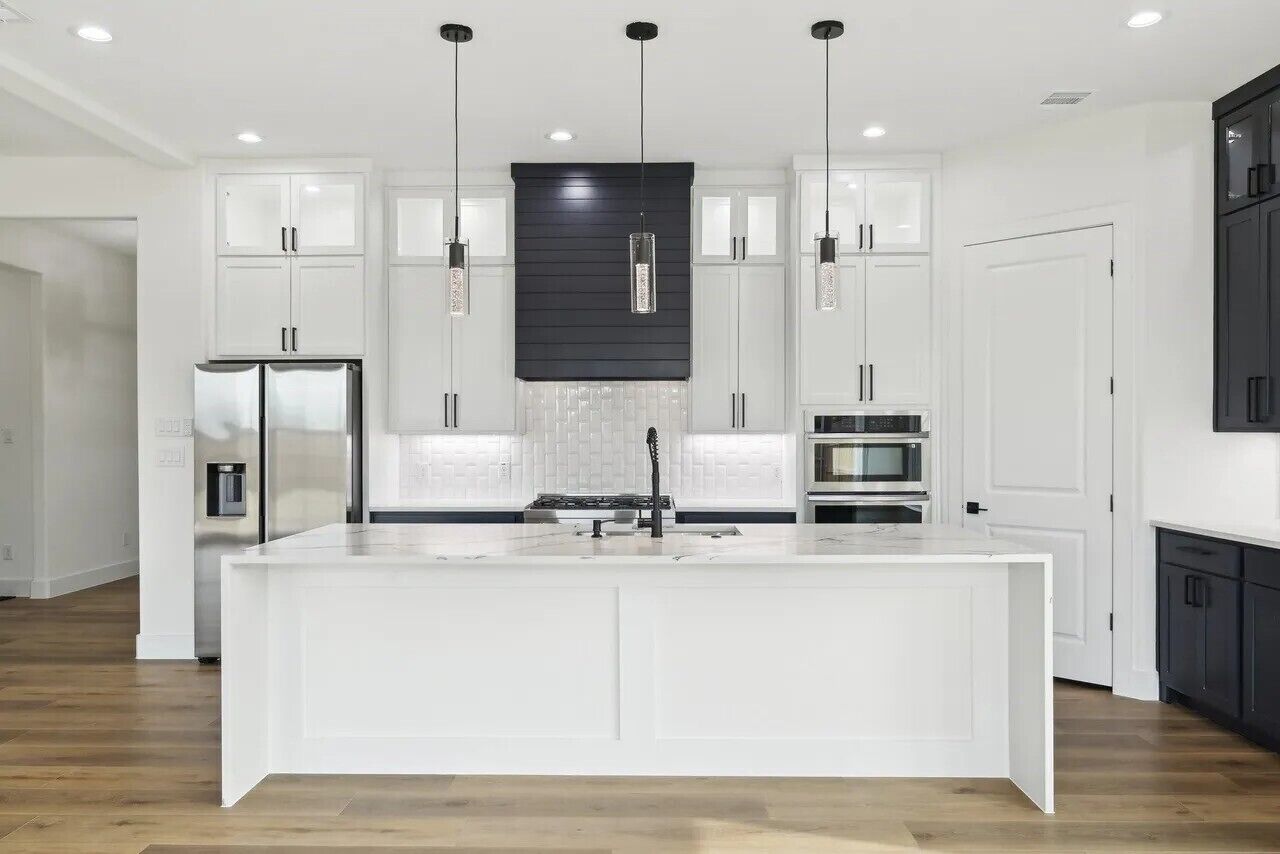 Cozinha moderna com armários brancos, uma ilha central e iluminação pendente.