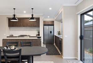 Et moderne køkken med spiseplads, med en central ø, hængende lamper og et rustfrit stål køleskab.