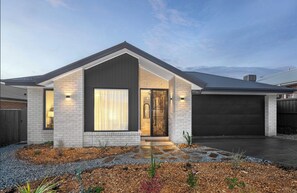 Et moderne hus i et plan med garage, en velholdt forhave med grus og træflis, samt et stort vindue ved hoveddøren.