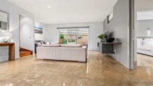Uma sala de estar moderna com um sofá grande, uma área de refeições com mesa de madeira e uma cozinha com bancada preta.