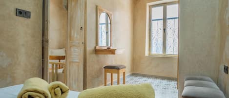 A room with a bed, a bench, a window, and a mirror.
