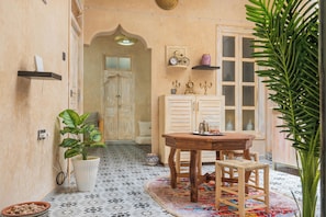 Een gezellige kamer met betegelde vloer, een houten tafel met stoelen, een kamerplant en een deur naar een andere ruimte.