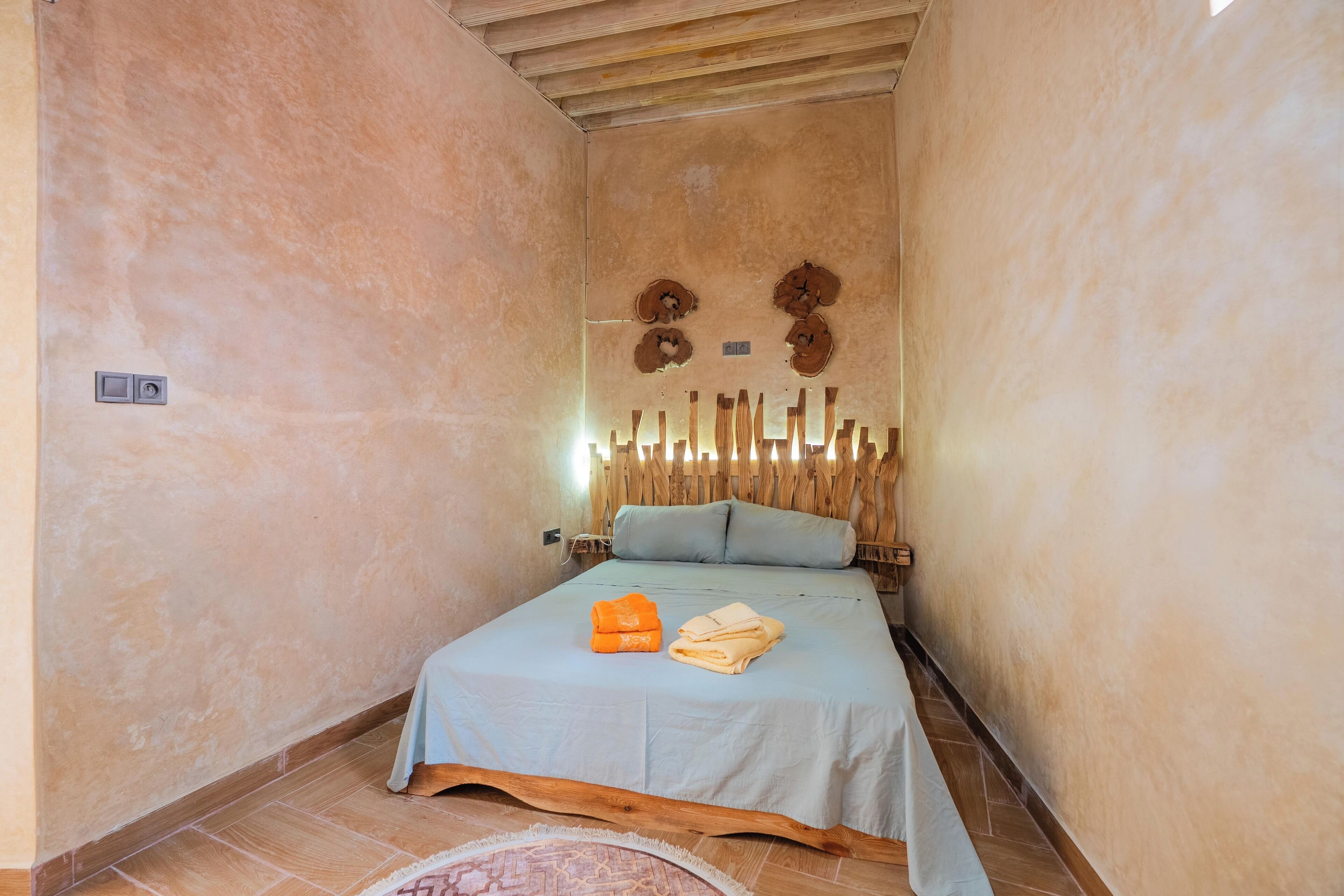A small, cozy room with a single bed, a wooden headboard, and a simple wall decor.