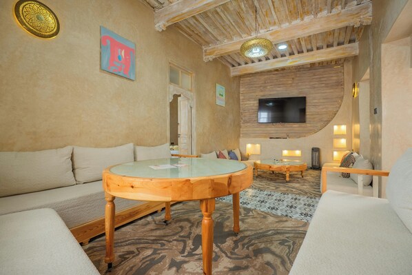 A modern living room with a glass-top coffee table, a sofa, a TV mounted on a wooden wall, and a patterned carpet.