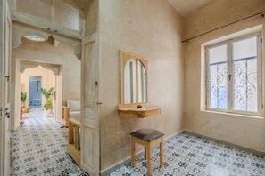 A room with a patterned floor, a wooden bench, a mirror, and a window with decorative bars. - Refuge Oriental: 2BR Medina Home with Private Copper Hammam (Essaouira)