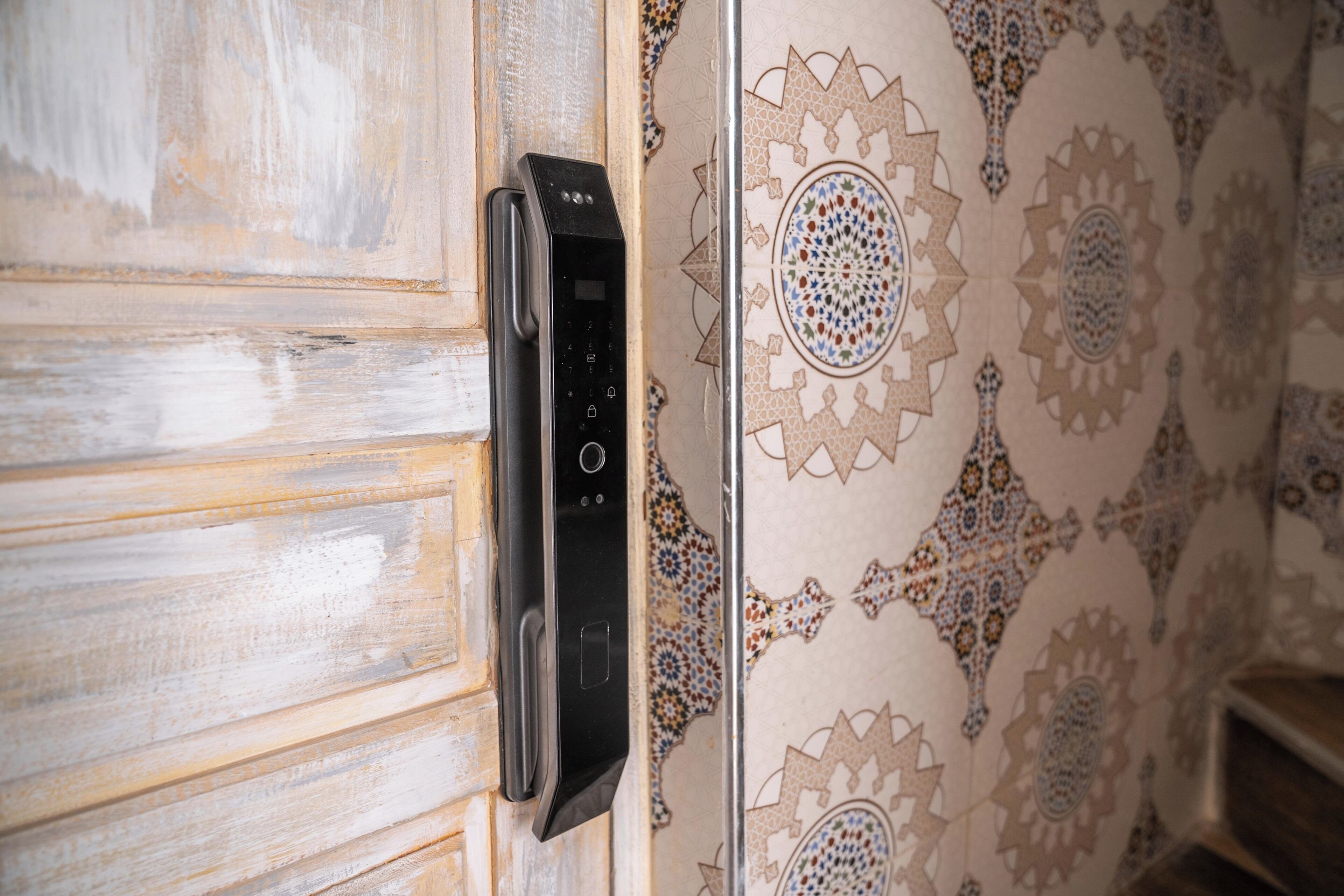 A door with a black intercom system and a wall with intricate tile patterns.