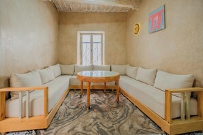 A cozy living room with a sectional sofa, a round glass-top coffee table, and a patterned rug. - Refuge Oriental: 2BR Medina Home with Private Copper Hammam (Essaouira)